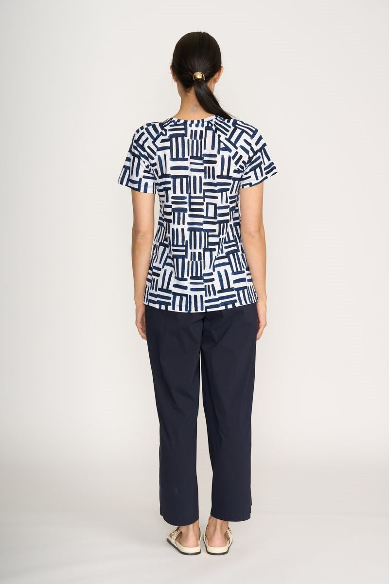 Person wearing a navy and white geometric patterned top with dark pants on a white background