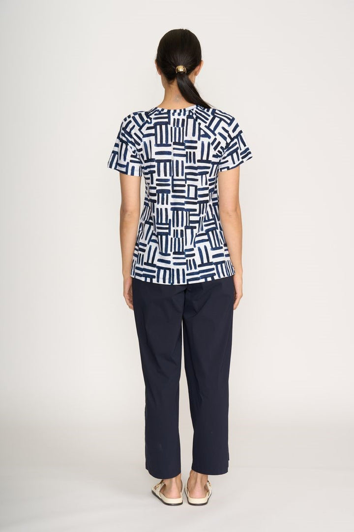 Person wearing a navy and white geometric patterned top with dark pants on a white background