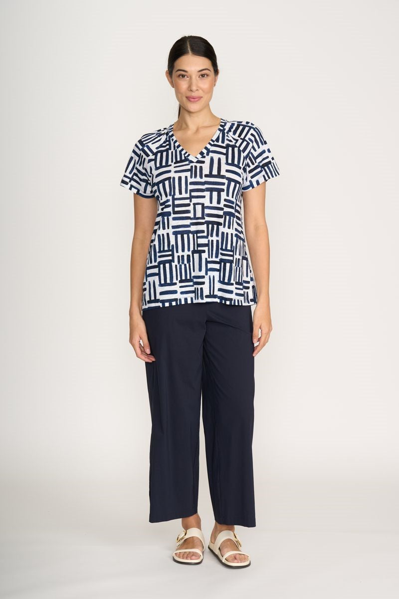 Woman wearing a black and white patterned top and navy pants on a white background