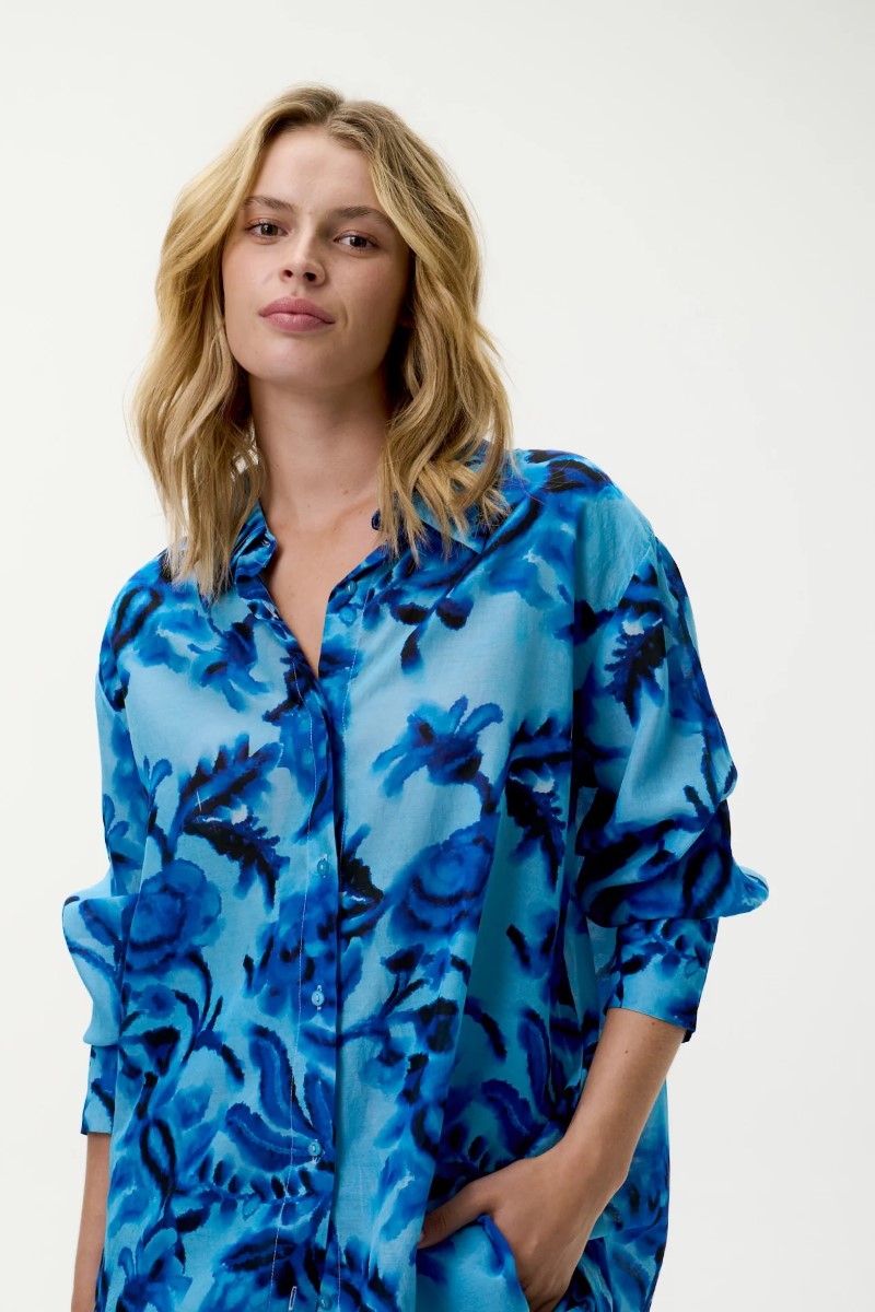 Woman wearing a blue floral patterned shirt against a white background