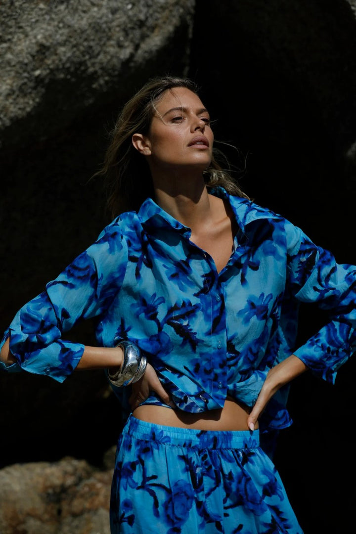 Woman wearing a blue floral outfit standing against a dark background