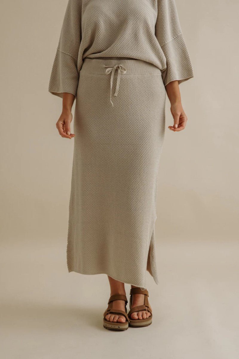 Person wearing a beige textured skirt and top on a plain background