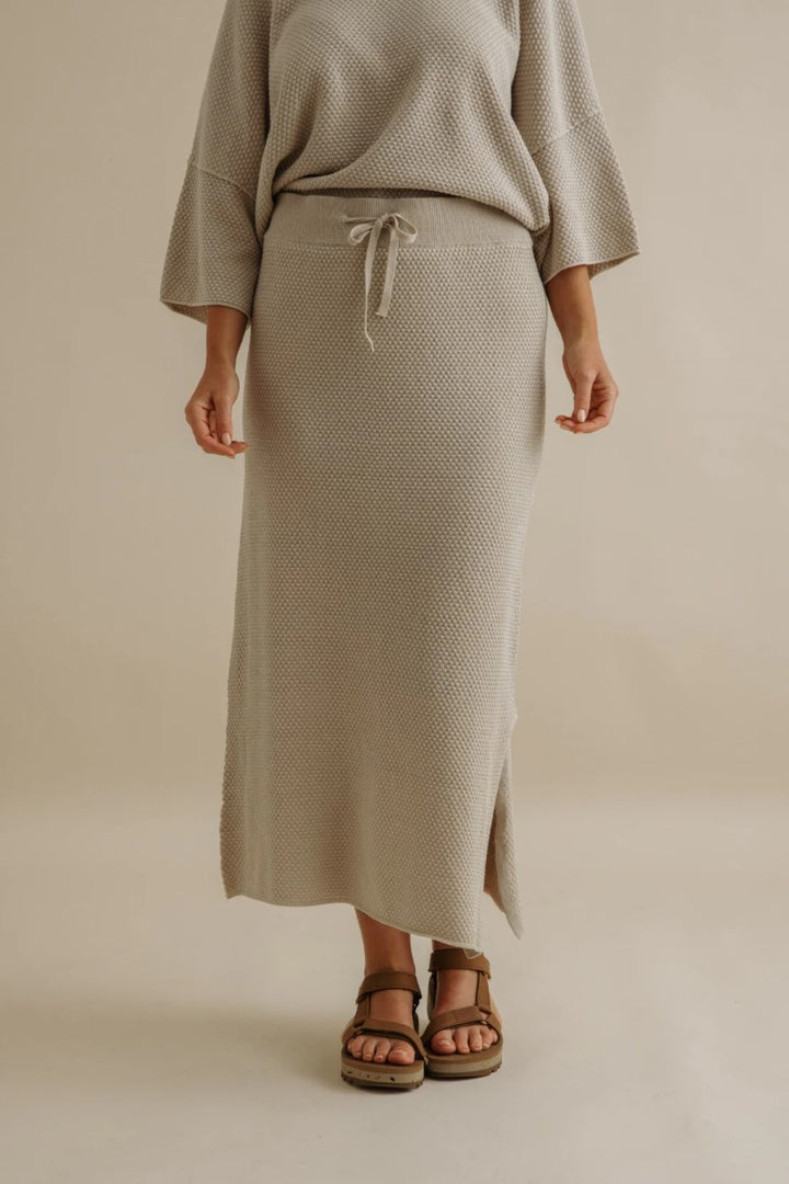 Person wearing a beige textured skirt and top on a plain background