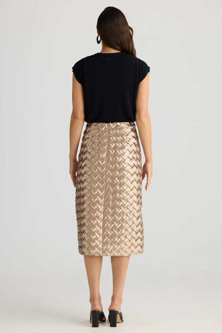 Woman wearing a black top and gold patterned skirt on a white background