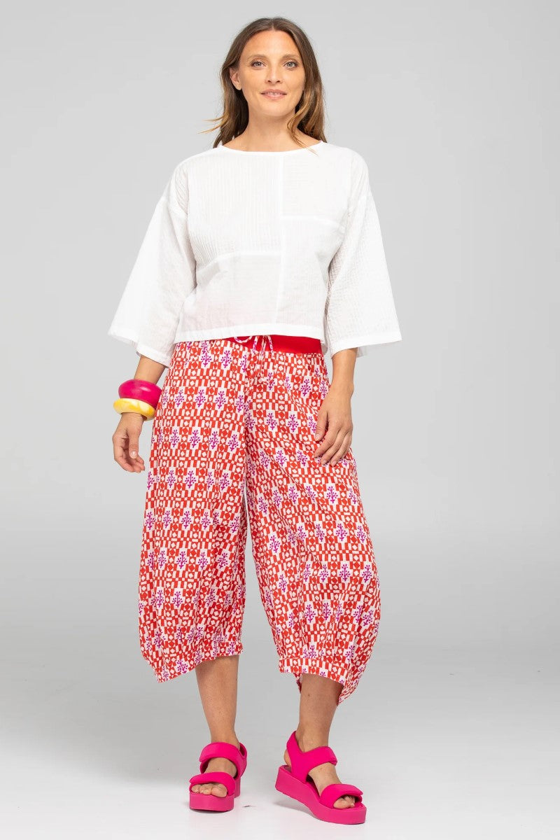 Woman wearing a white top and red patterned pants on a gray background
