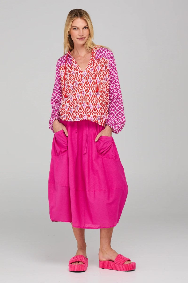 Woman wearing a patterned top and bright pink skirt on a plain background