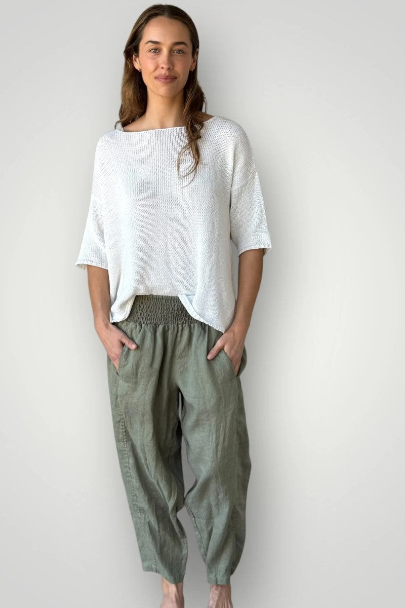 Woman wearing a white top and green pants against a plain background