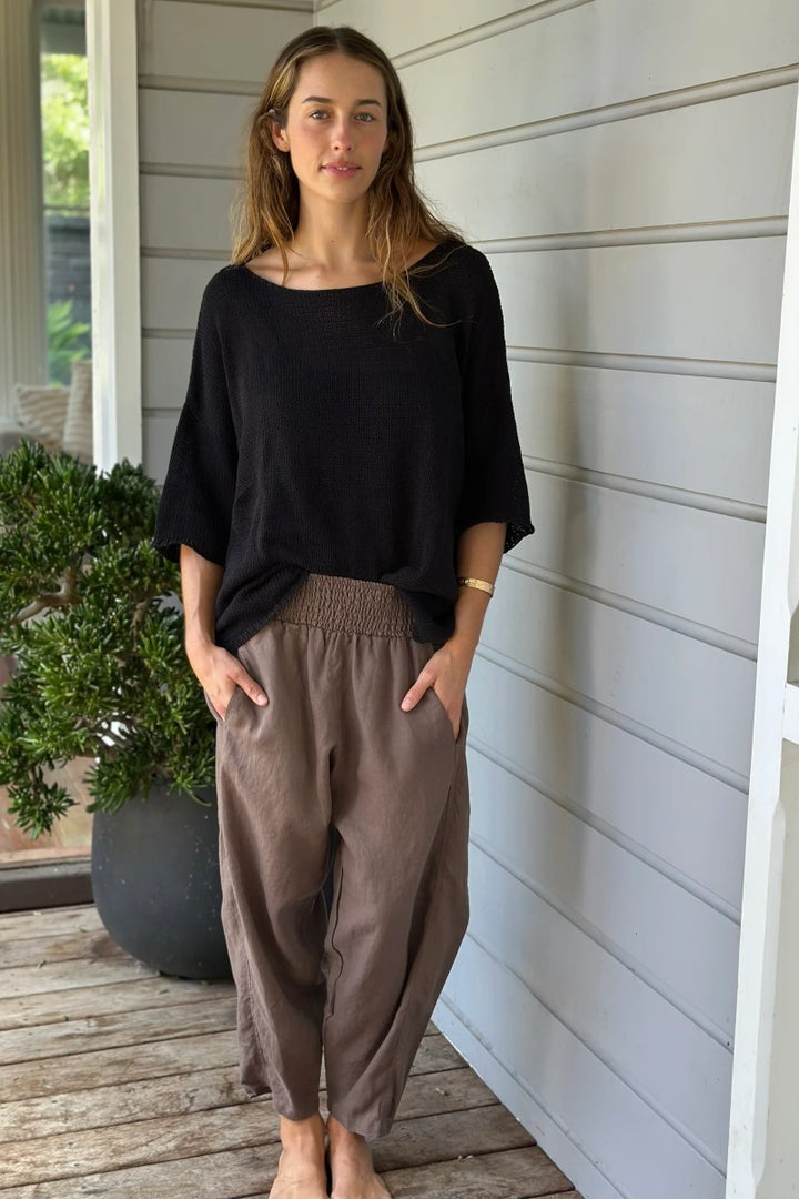 Woman wearing a black top and brown pants standing on a wooden deck.