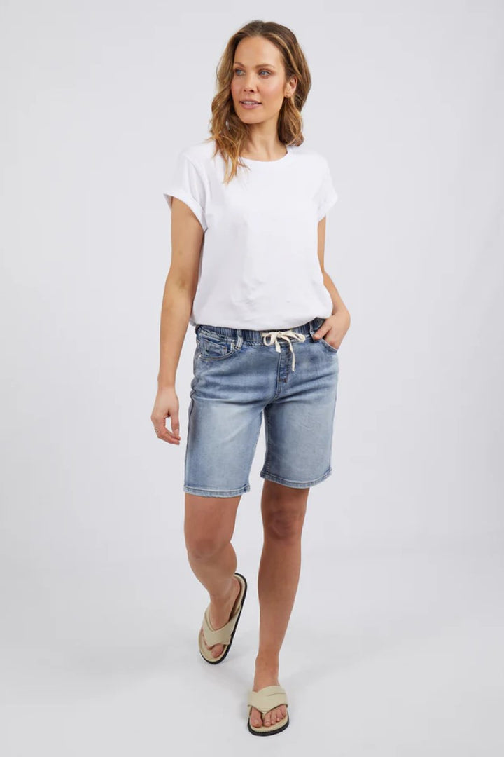 Woman wearing a white t-shirt and denim shorts on a plain background