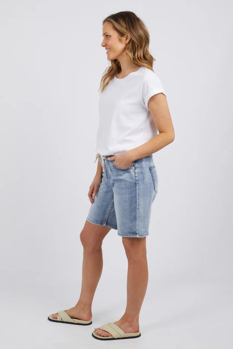 Woman wearing a white t-shirt and light blue denim shorts on a plain background