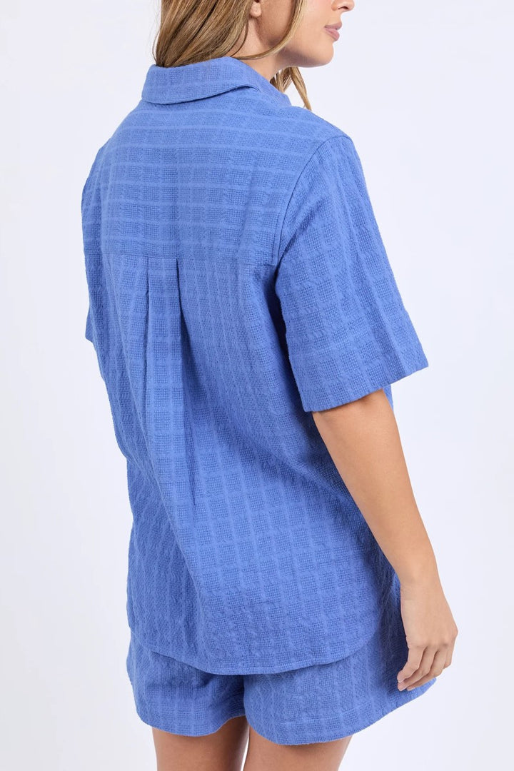 Woman wearing a blue checkered shirt and shorts set on a white background