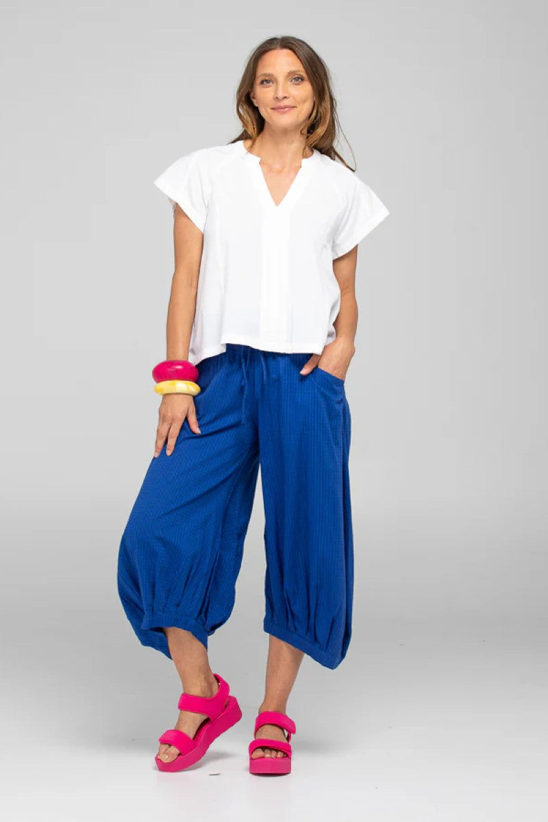 Woman wearing a white top and blue pants with pink sandals on a gray background