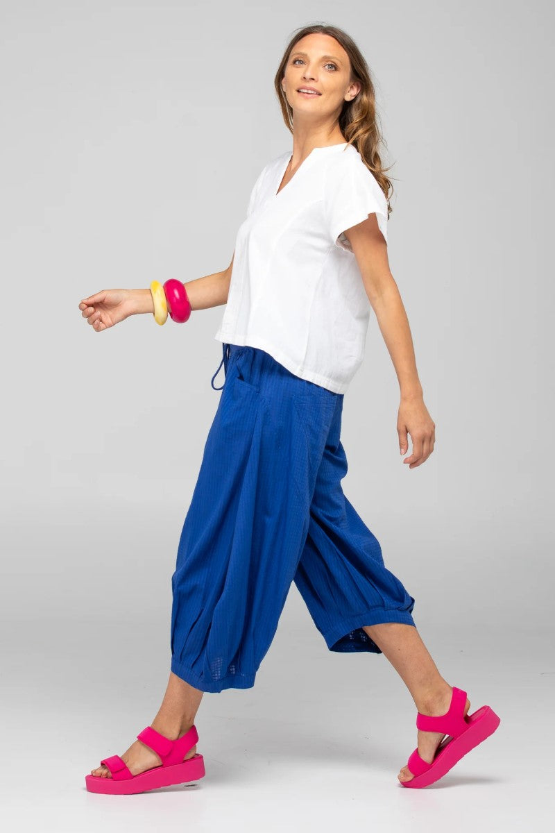Woman wearing a white top and blue pants with pink sandals on a gray background