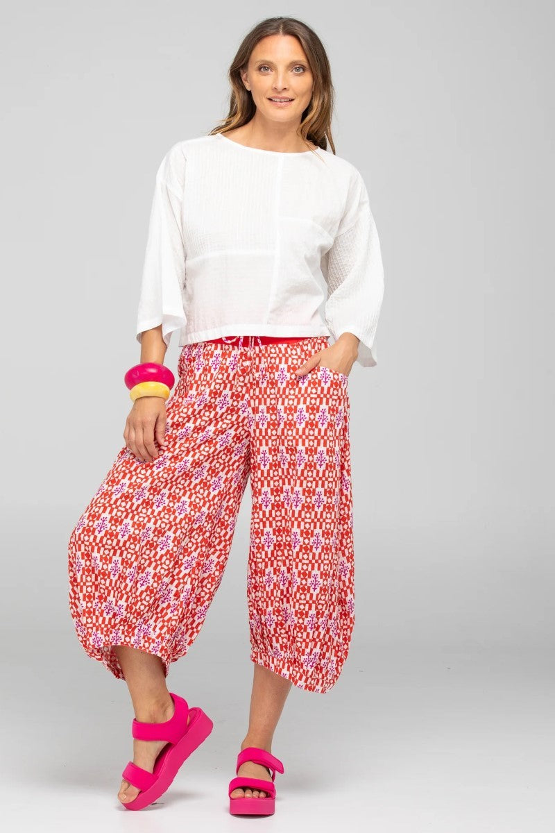 Woman wearing a white top and red patterned pants on a gray background