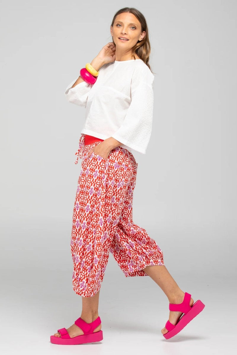 Woman wearing a white top and red floral pants with pink sandals on a gray background