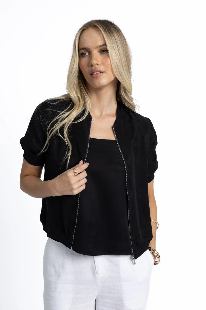 Woman wearing a black jacket over a black top with white pants on a white background