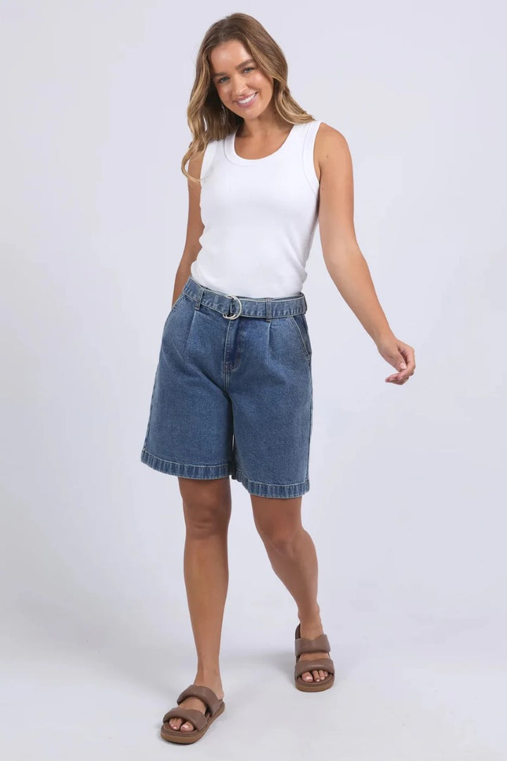 Woman wearing a white sleeveless top and blue denim shorts on a white background