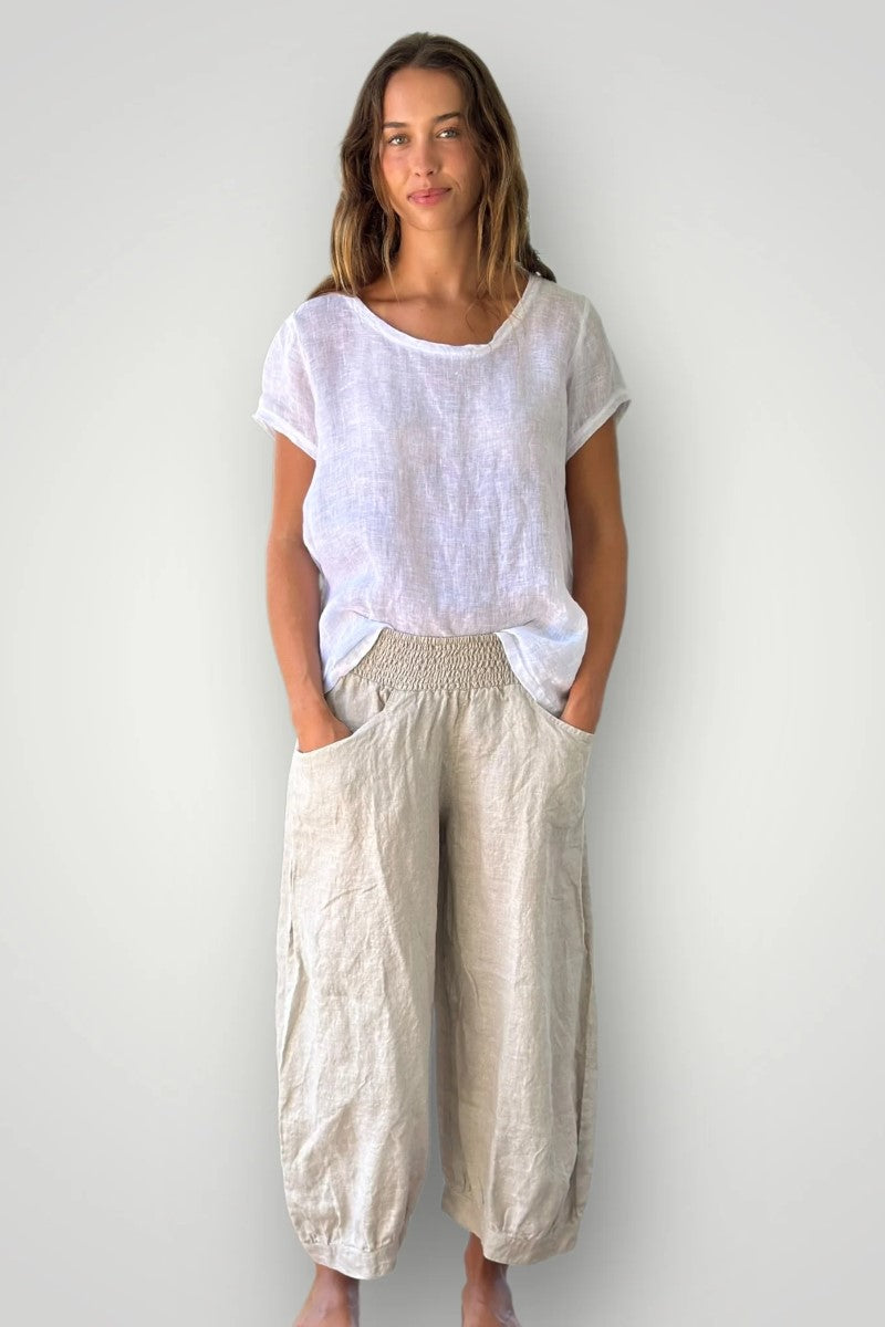Woman wearing a white top and beige pants against a plain background