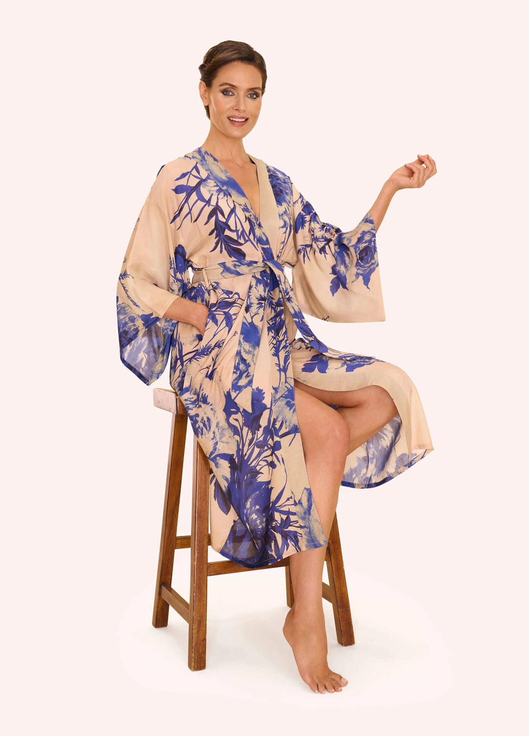 Woman wearing a floral robe sitting on a stool against a white background