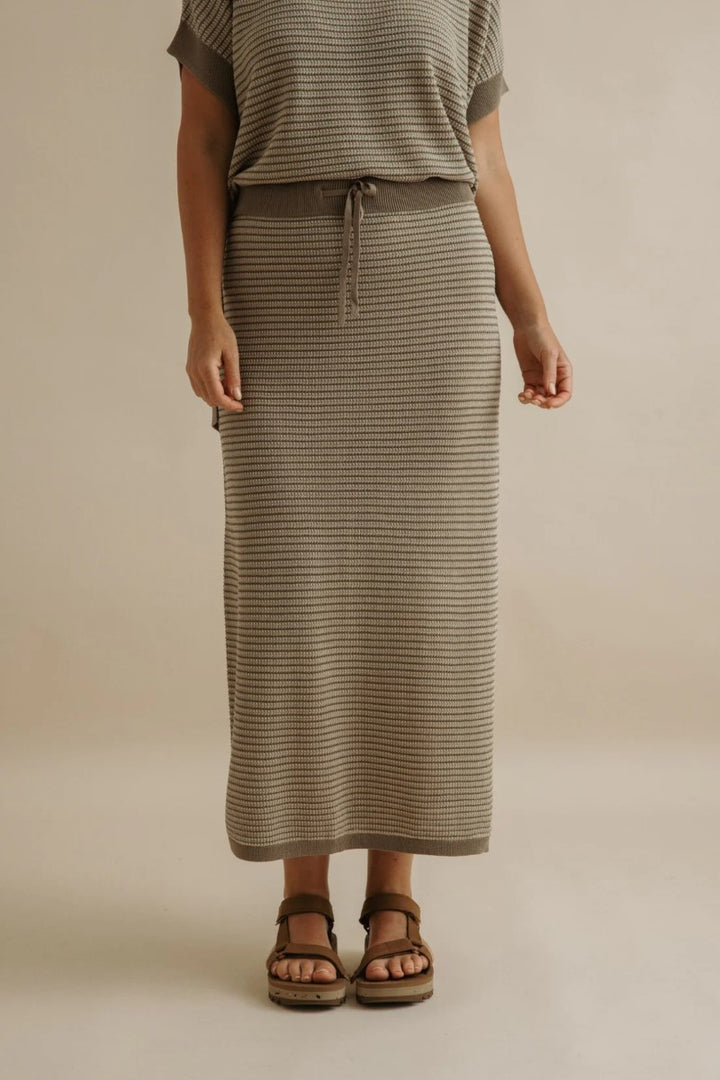 Person wearing a striped skirt and top on a beige background