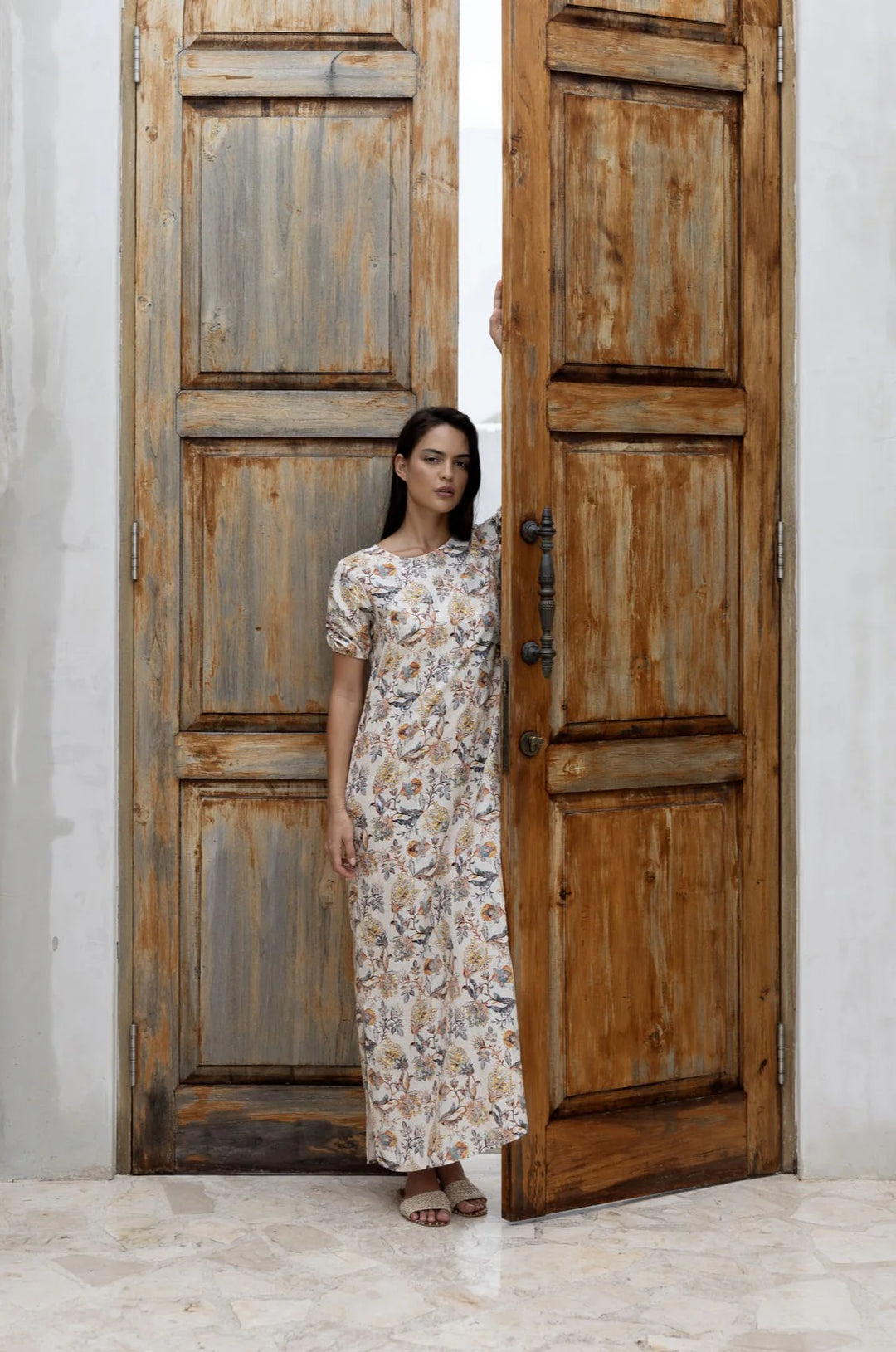 Woman in a floral dress standing in front of a large wooden door.