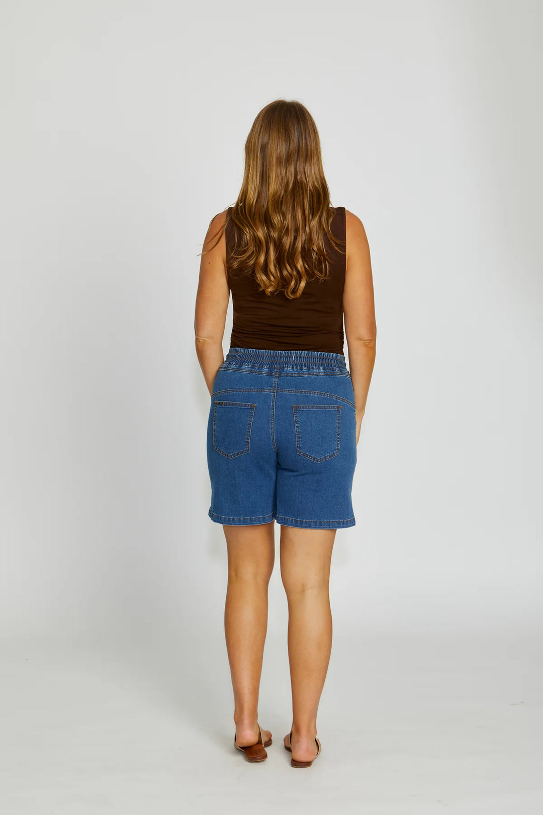 Person wearing a brown sleeveless top and blue denim shorts on a white background