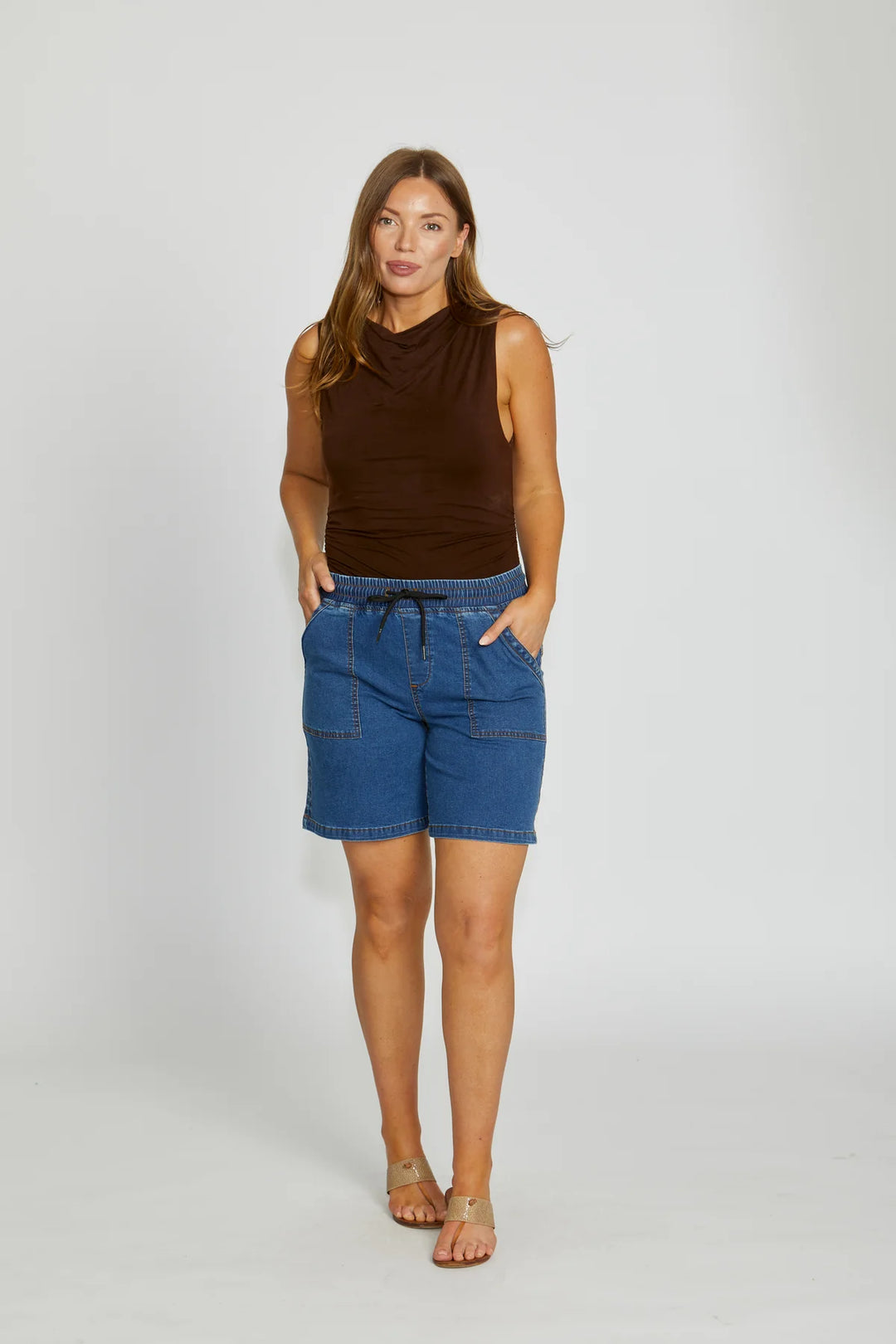 Woman wearing a brown sleeveless top and blue denim shorts on a white background