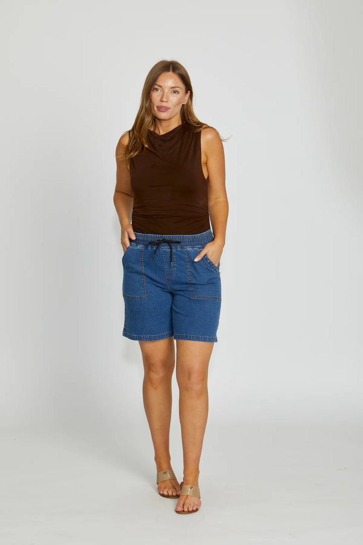 Woman wearing a brown sleeveless top and blue denim shorts on a white background