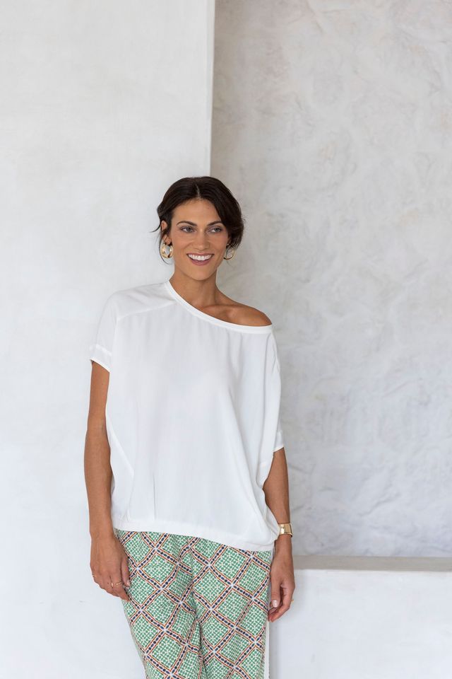 Woman wearing a white top and patterned pants against a plain wall