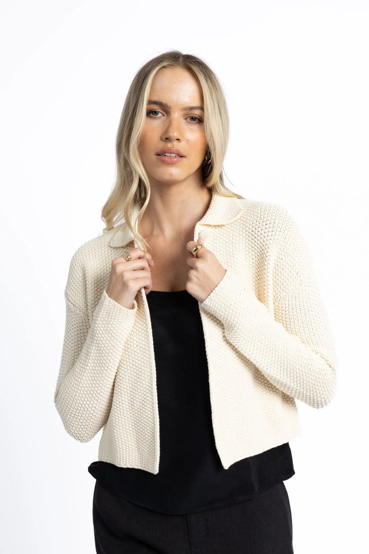 Woman wearing a cream cardigan over a black top on a white background