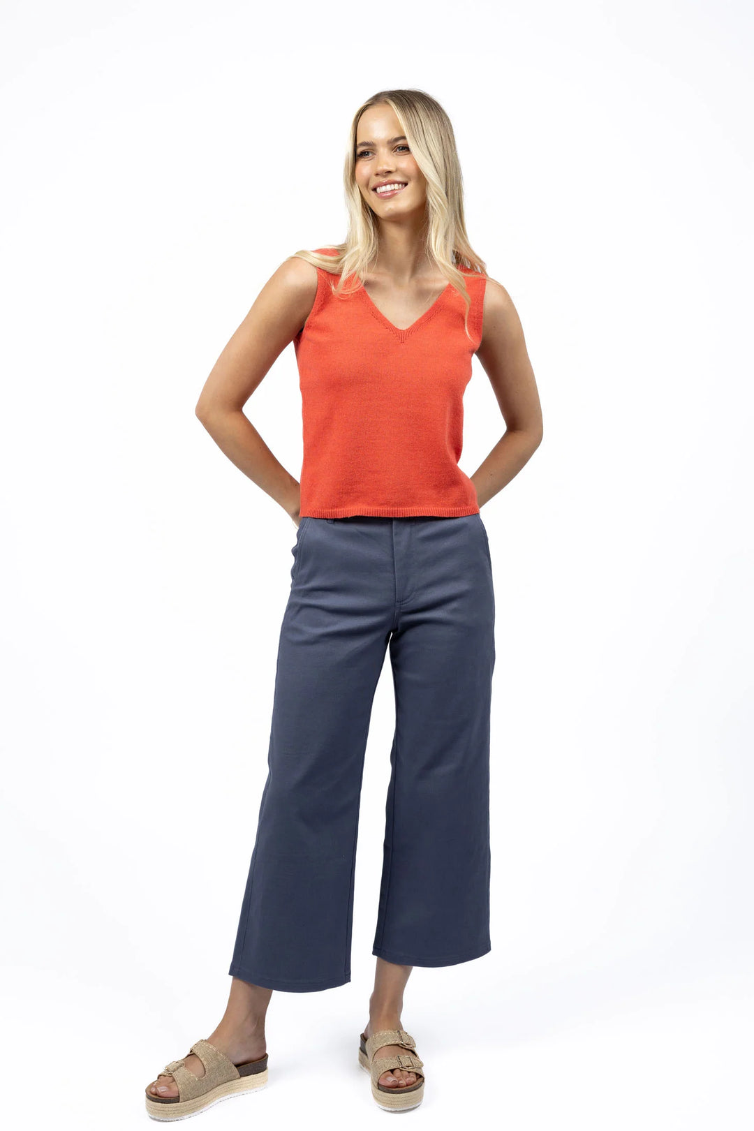 Woman wearing an orange tank top and blue pants on a white background
