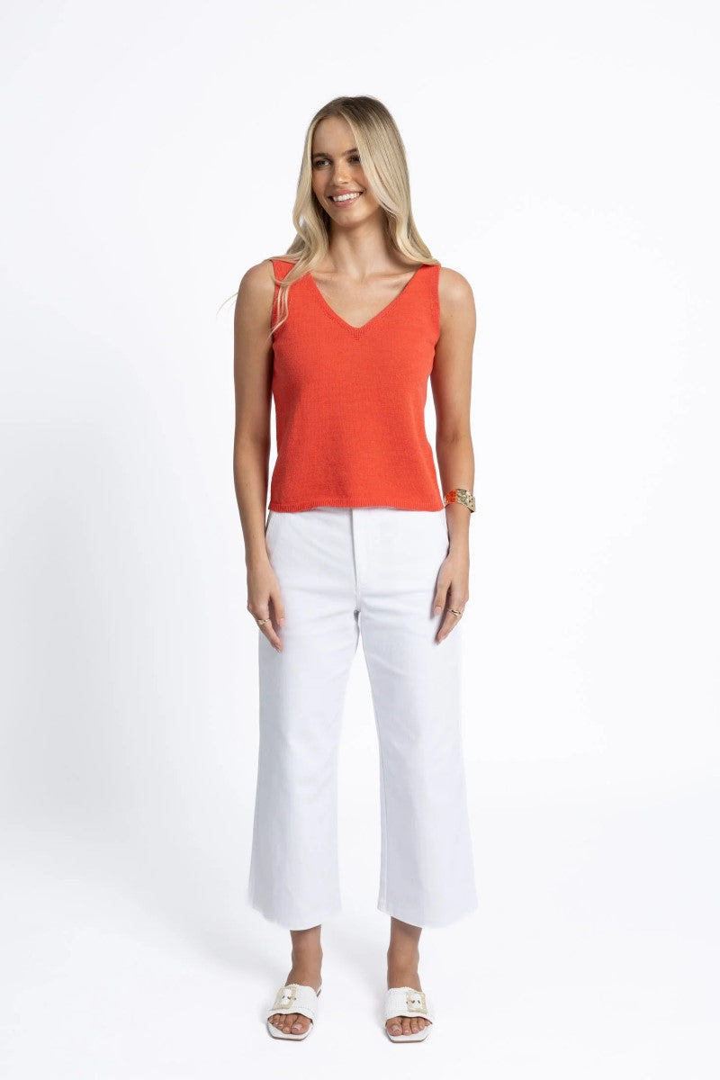 Woman wearing an orange sleeveless top and white pants on a white background