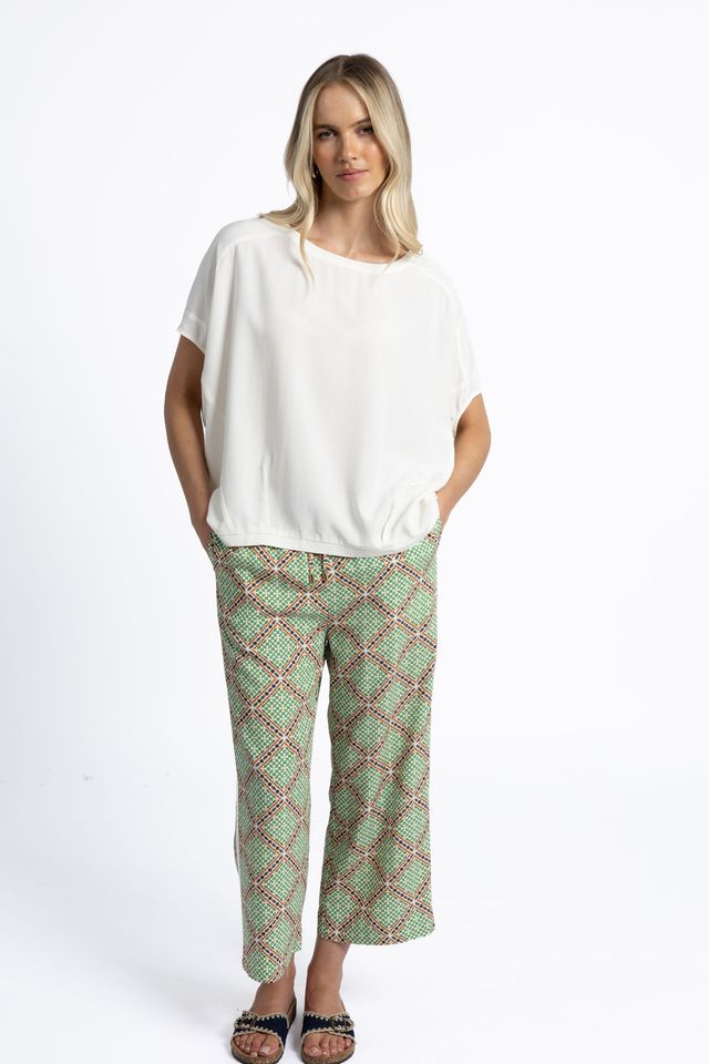 Woman wearing a white top and green patterned pants on a white background