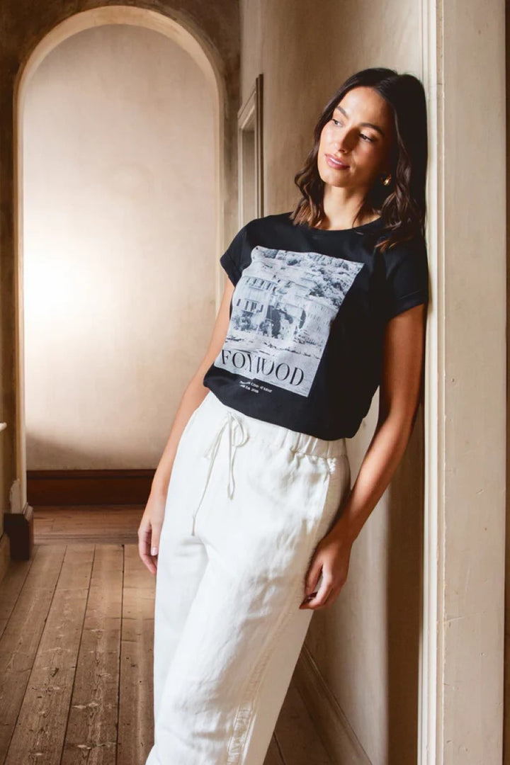 Woman wearing a black t-shirt with graphic design and white pants in an indoor setting