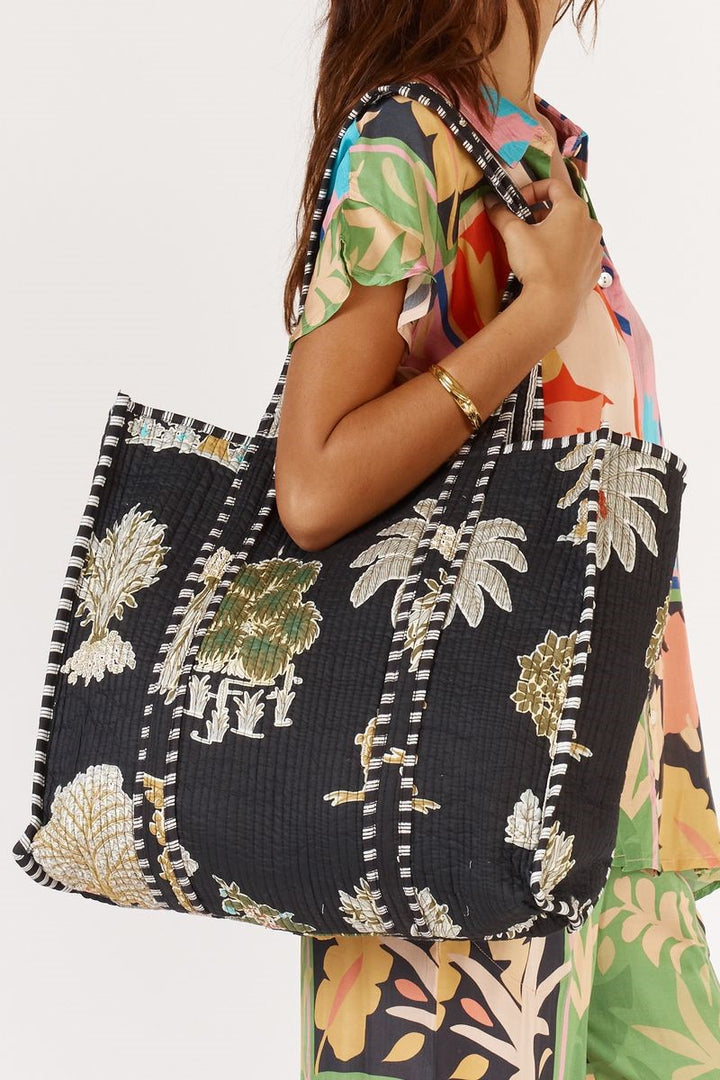Person holding a black tote bag with tropical leaf patterns against a white background