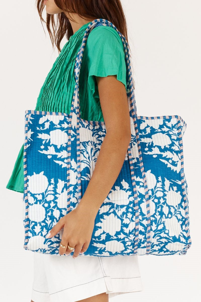 Person holding a blue floral tote bag against a white background