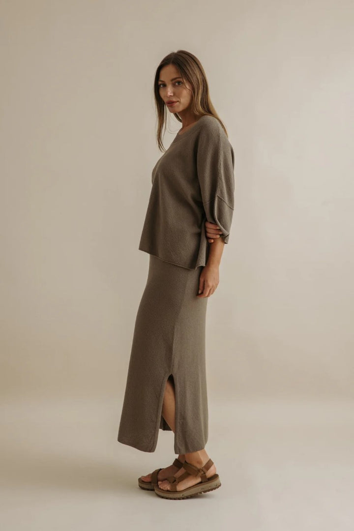 Woman wearing a matching olive green outfit with a slit skirt on a beige background