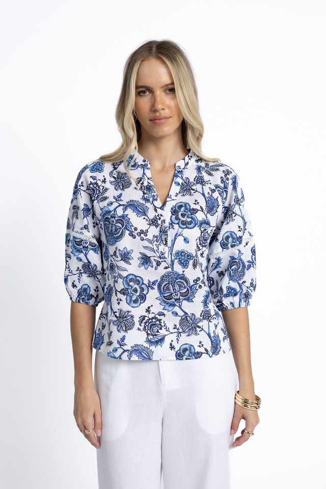 Woman wearing a blue floral blouse and white pants on a white background