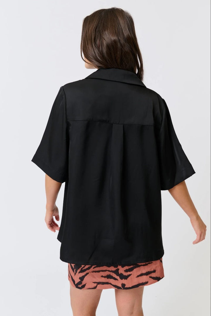 Person wearing a black oversized shirt over a patterned skirt on a white background