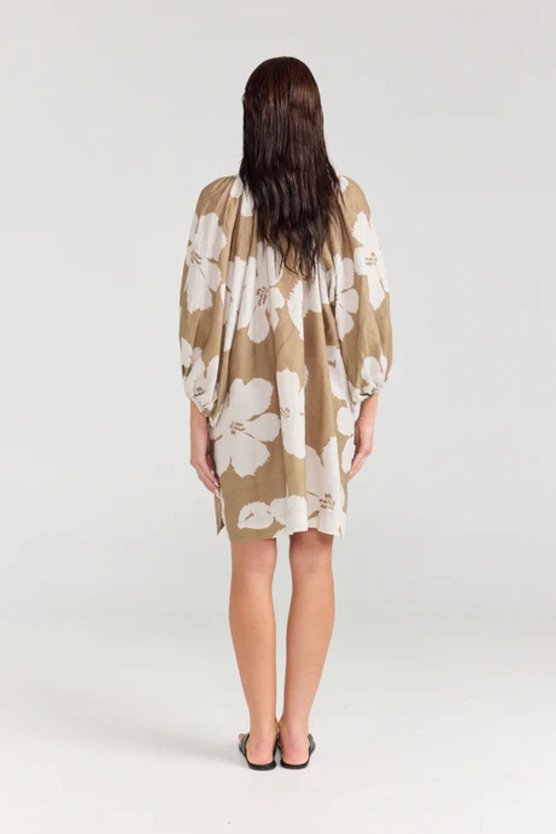 Woman wearing a beige kimono-style dress with white floral patterns on a plain background