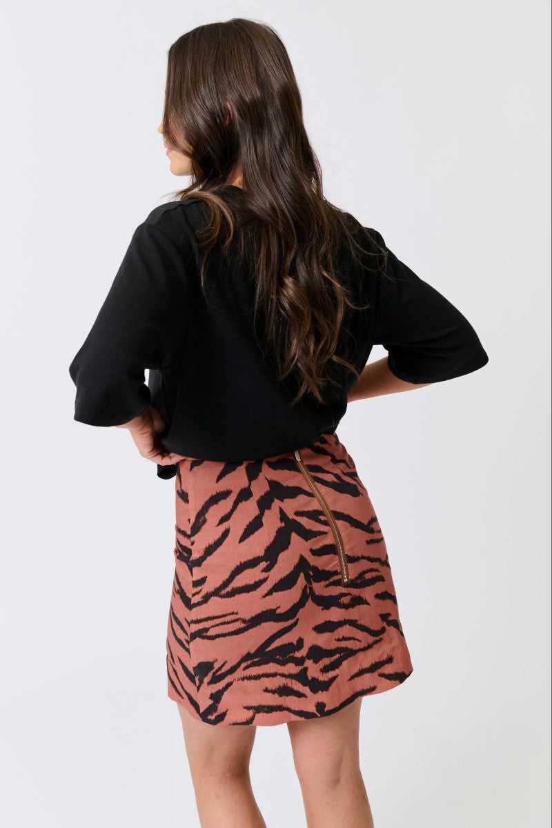 Person wearing a black top and pink tiger print skirt on a white background