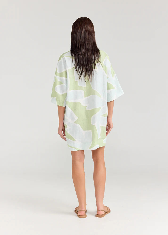 Woman wearing a light green and white patterned dress on a plain background