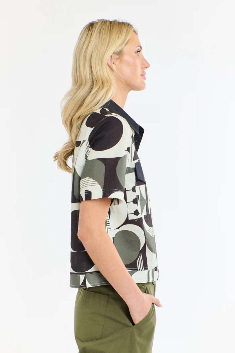 Woman wearing a patterned shirt and green pants on a white background
