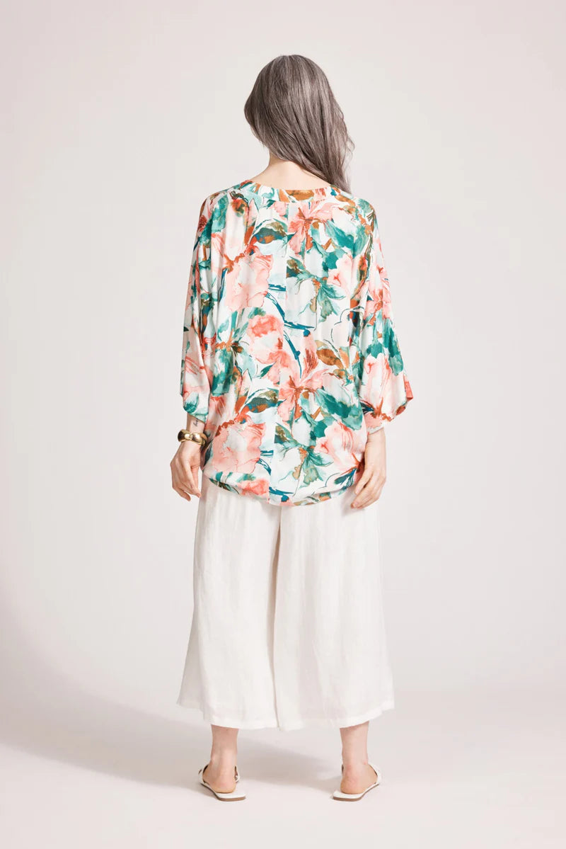 Person wearing a floral blouse and white pants on a plain background