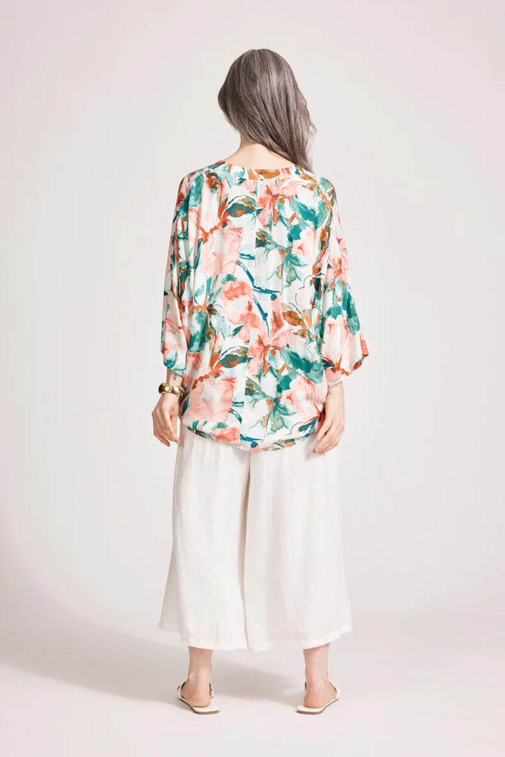 Person wearing a floral blouse and white pants on a plain background