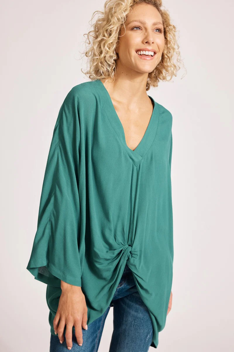 Woman wearing a teal poncho with a knot detail on a white background