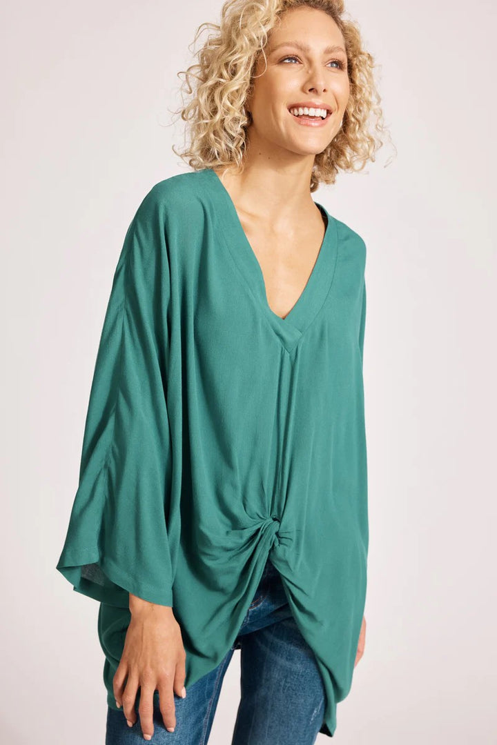 Woman wearing a teal poncho with a knot detail on a white background