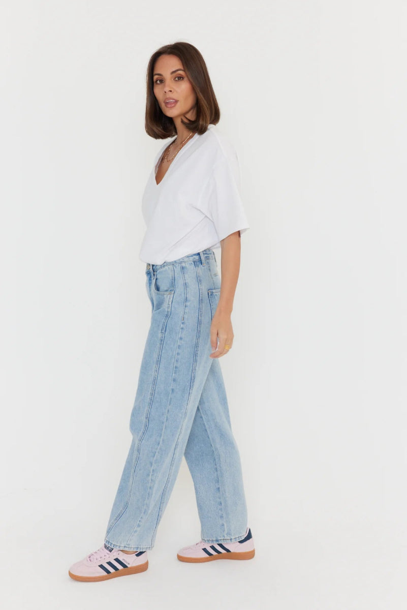 Woman wearing a white shirt and light blue jeans with Adidas shoes on a white background