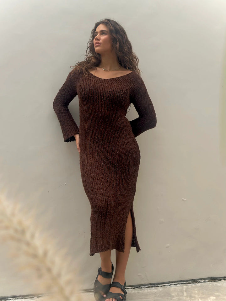 Woman standing in brown knit midi dress with side slit.