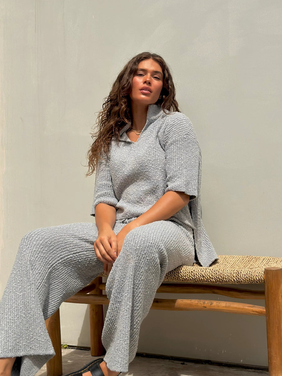 Woman seated on bench in gray knit lounge set.